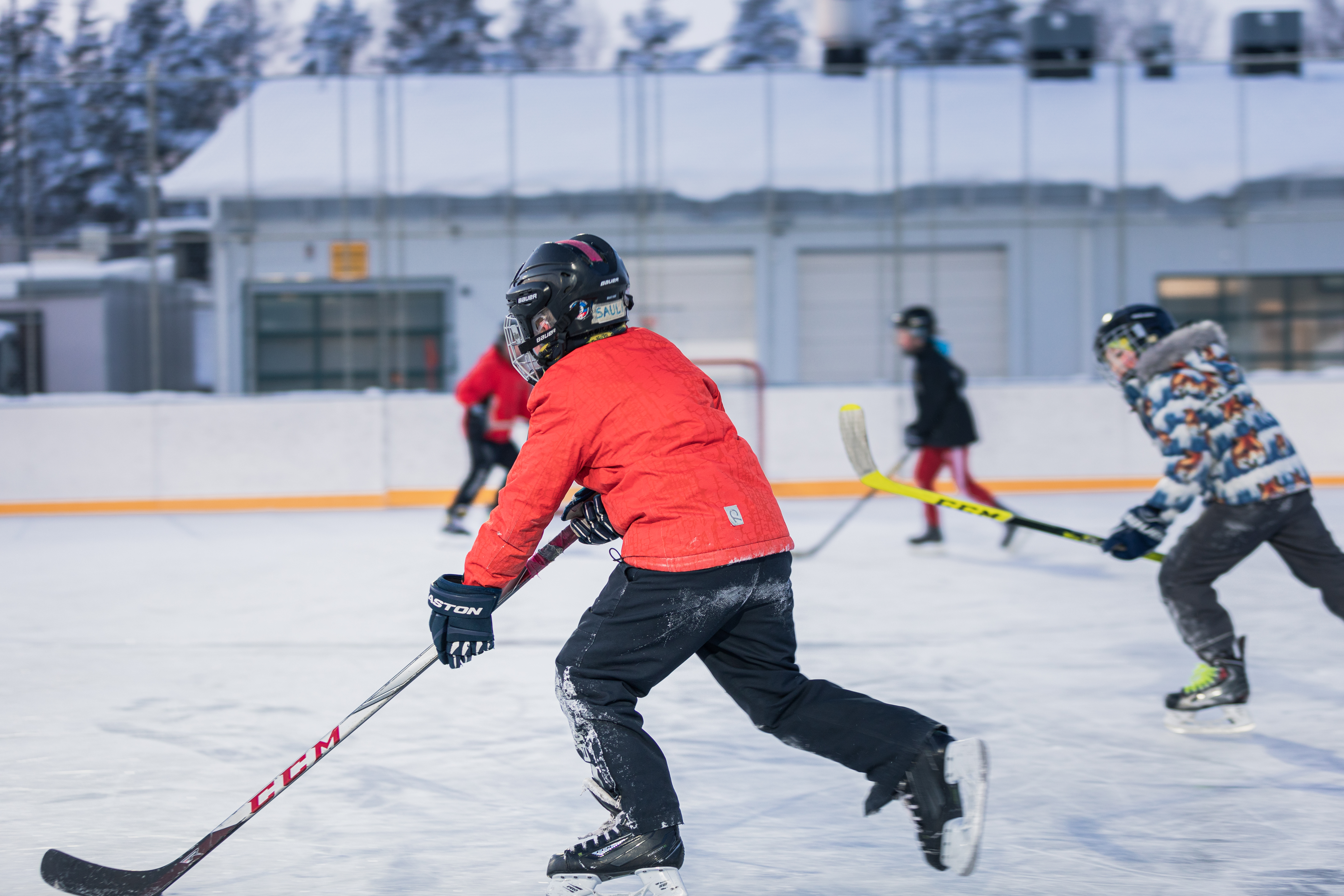 Lapset pelaavat jääkiekkoa kaukalossa.